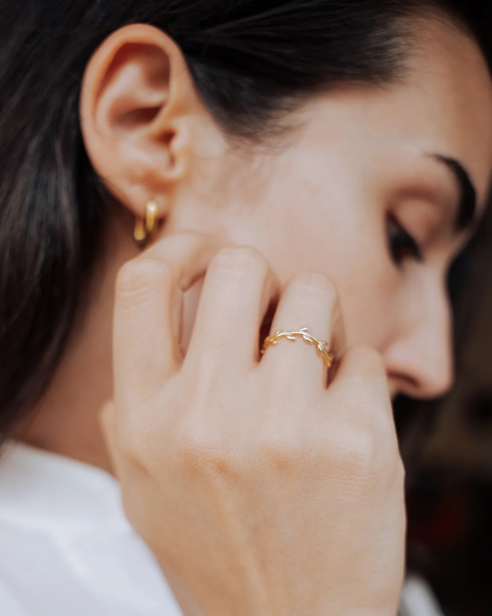 Anillo de hojas en plata de ley 925 con baño de oro puesto en la mano, junto a un aro dorado