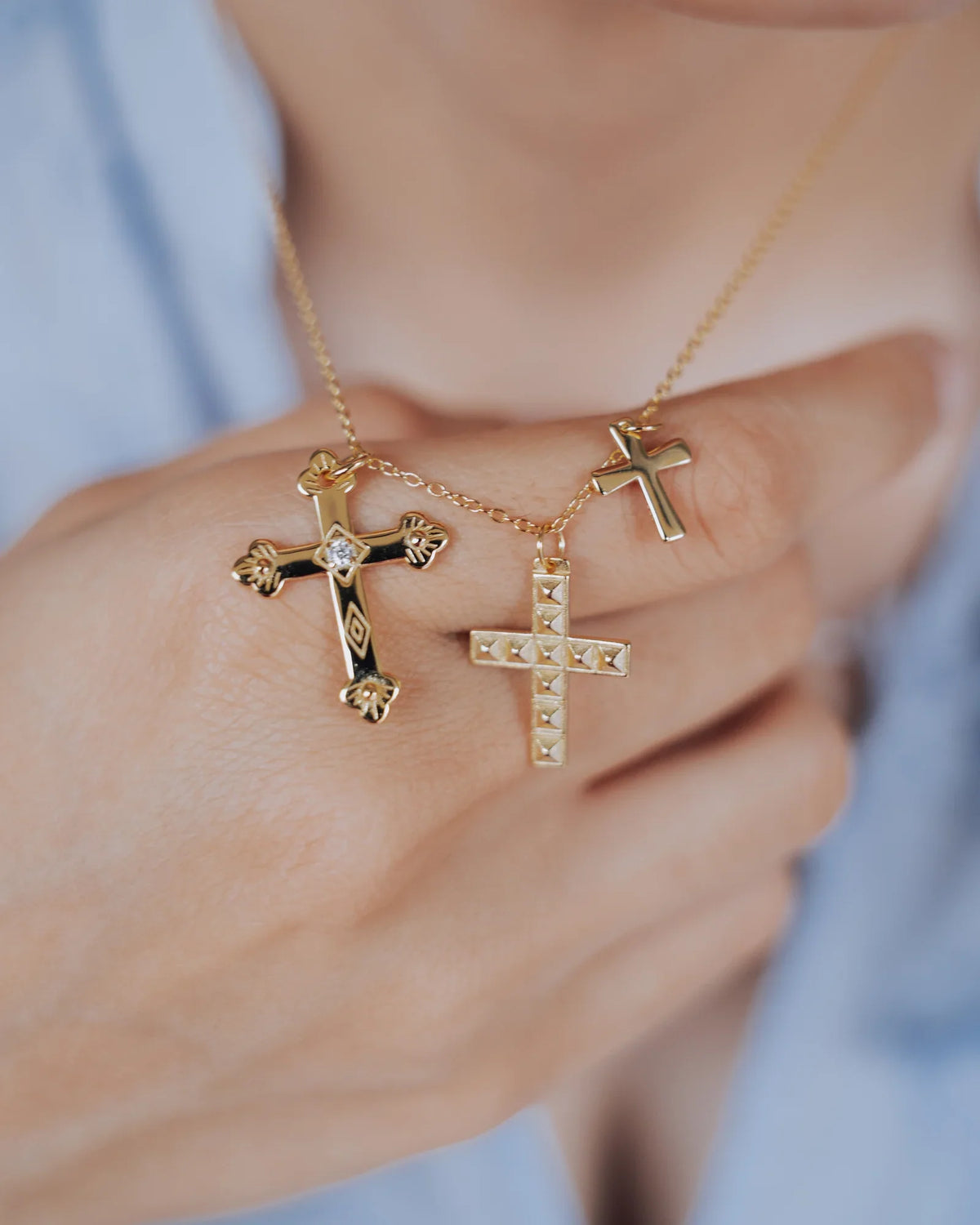 Collar de tres cruces en plata y dorado llevado sobre una camisa azul claro