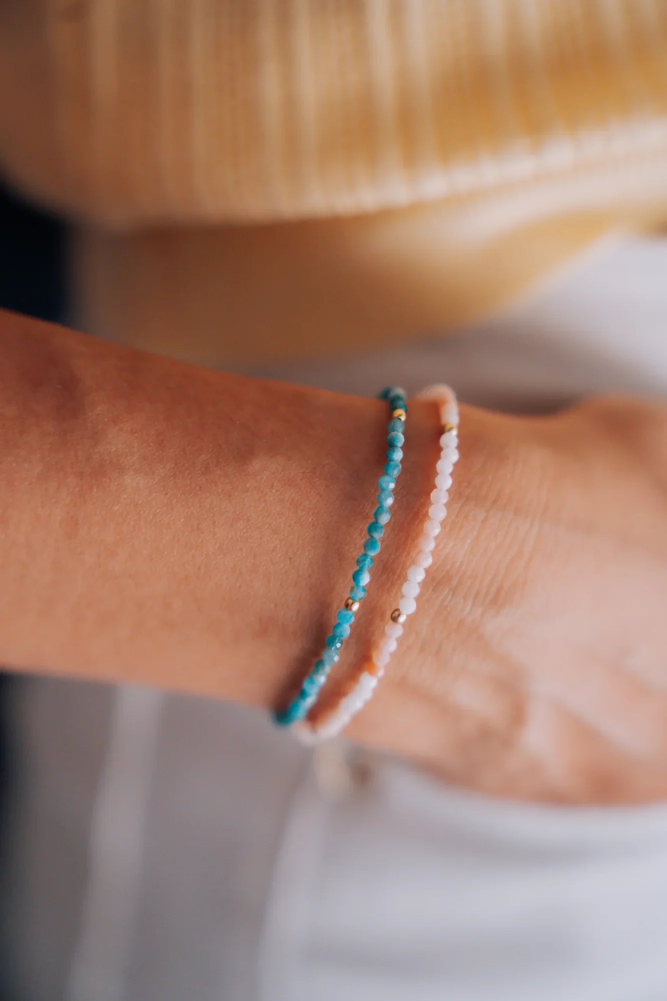 Dos pulseras de piedras naturales, opalo rosa y apatita, puestas en la muneca sobre un jersey amarillo