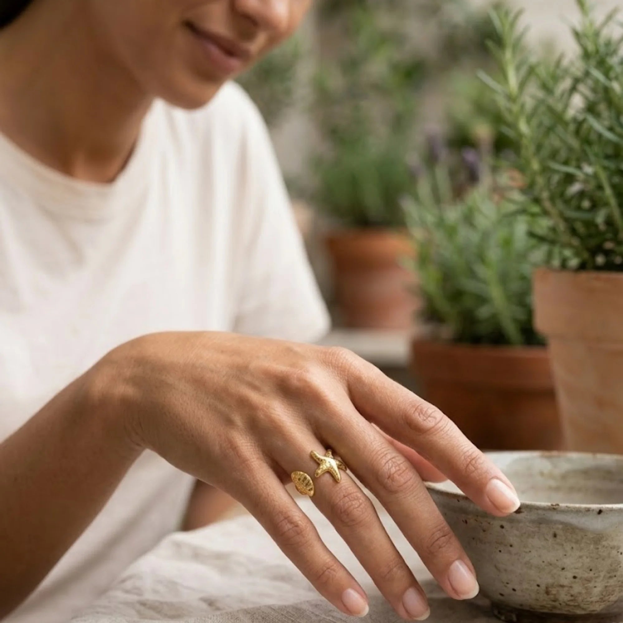 Mano con anillo abierto dorado de estrella de mar y concha junto a una taza