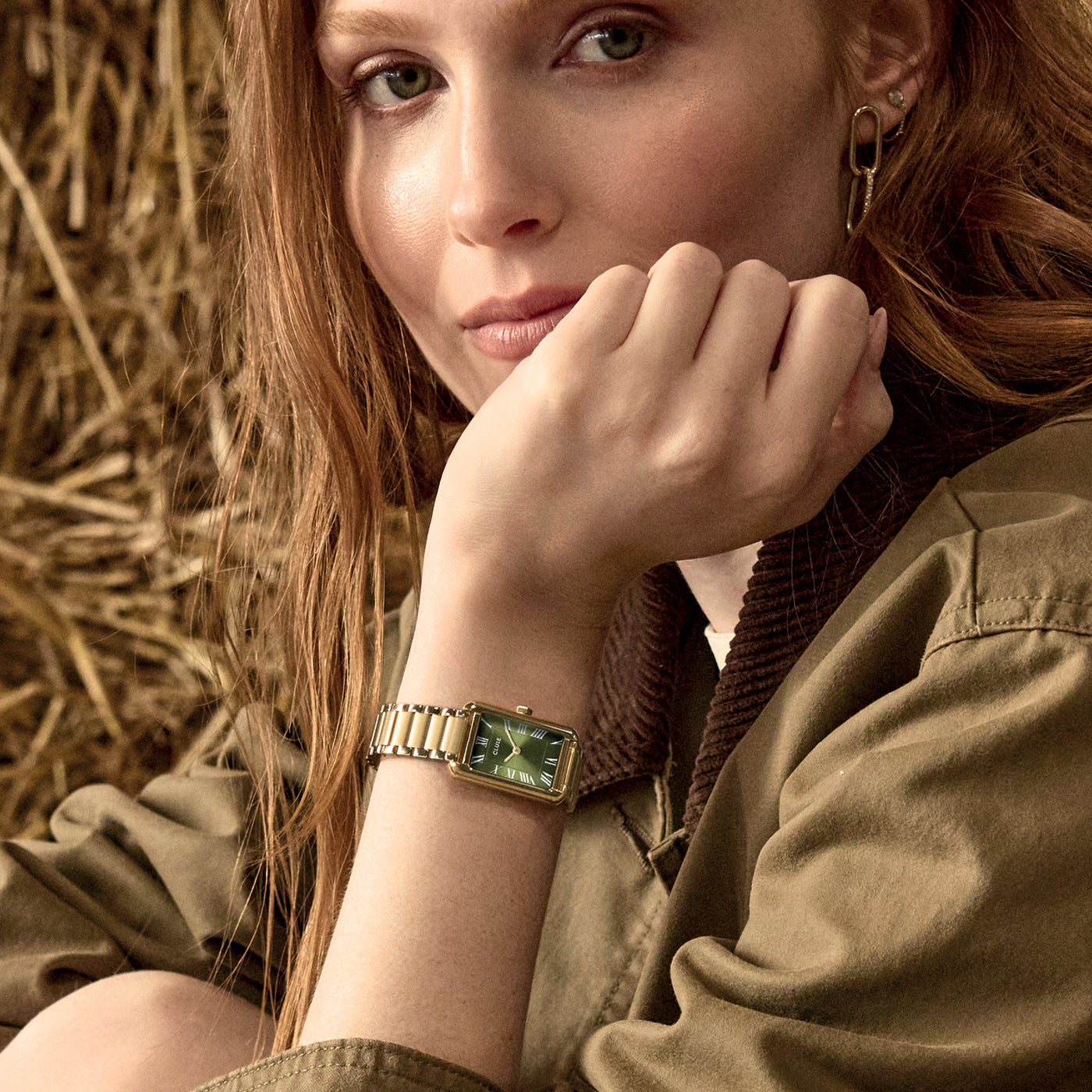 Modelo con reloj CLUSE Belisenna verde oliva y dorado en muñeca, estética editorial en exterior