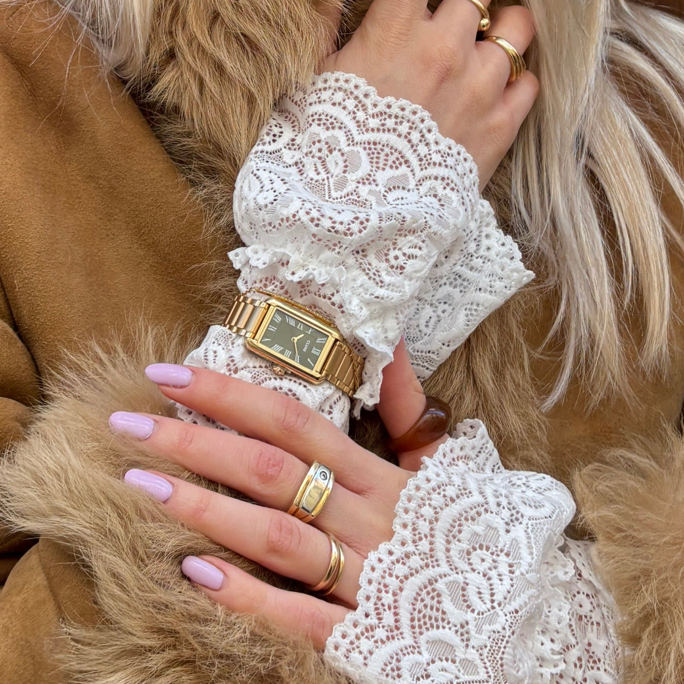 Reloj CLUSE Belisenna verde oliva y dorado en muñeca, combinado con abrigo camel y estilo elegante.