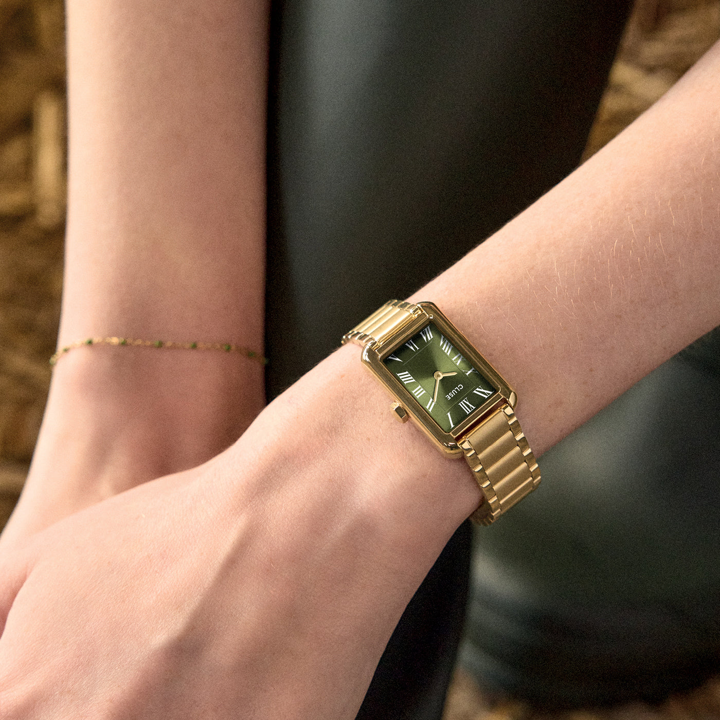 Primer plano del reloj CLUSE Belisenna verde oliva y dorado en muñeca, con pulsera fina al lado.