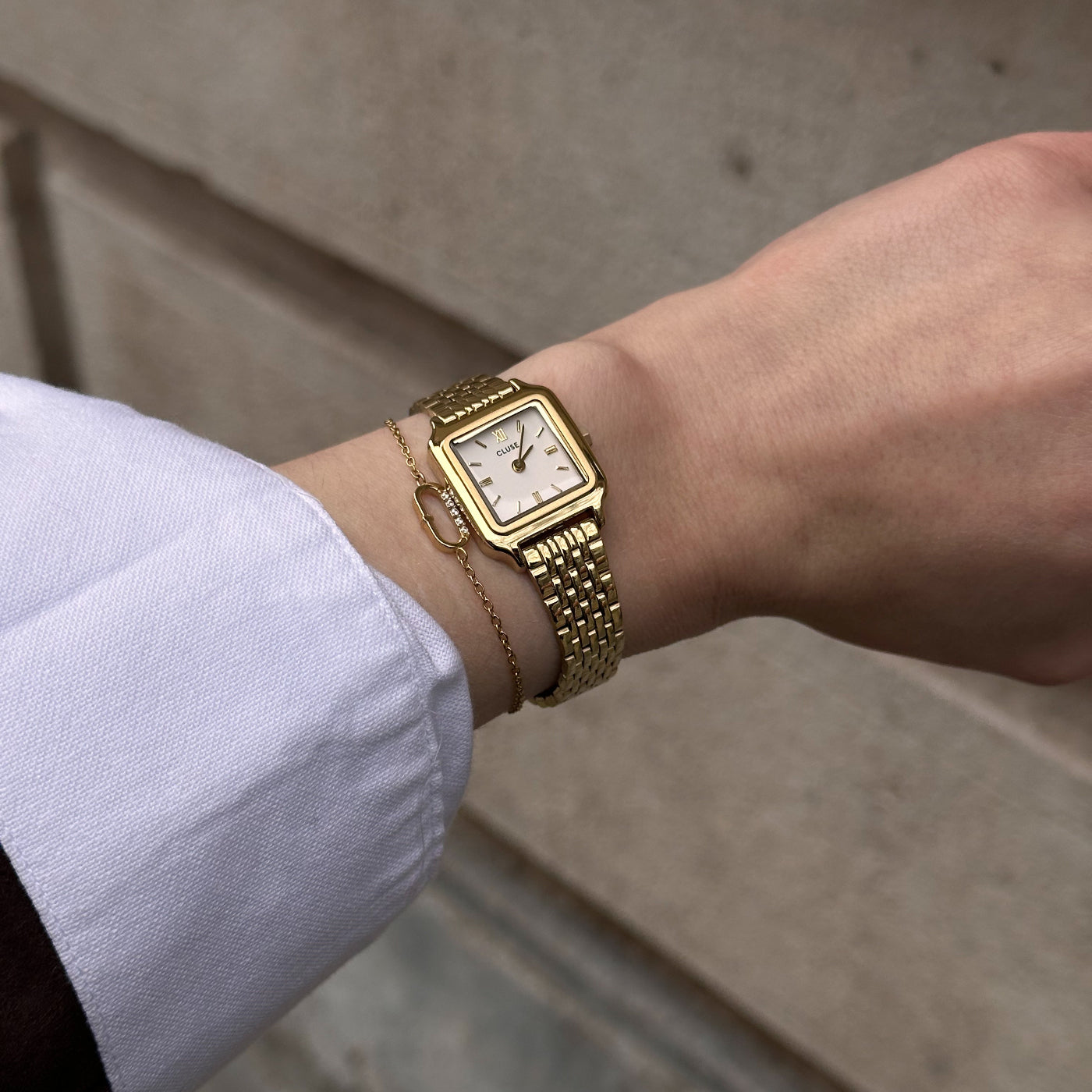 Primer plano del reloj CLUSE Gracieuse Mini dorado con esfera blanca, puesto en la muñeca junto a una pulsera fina.