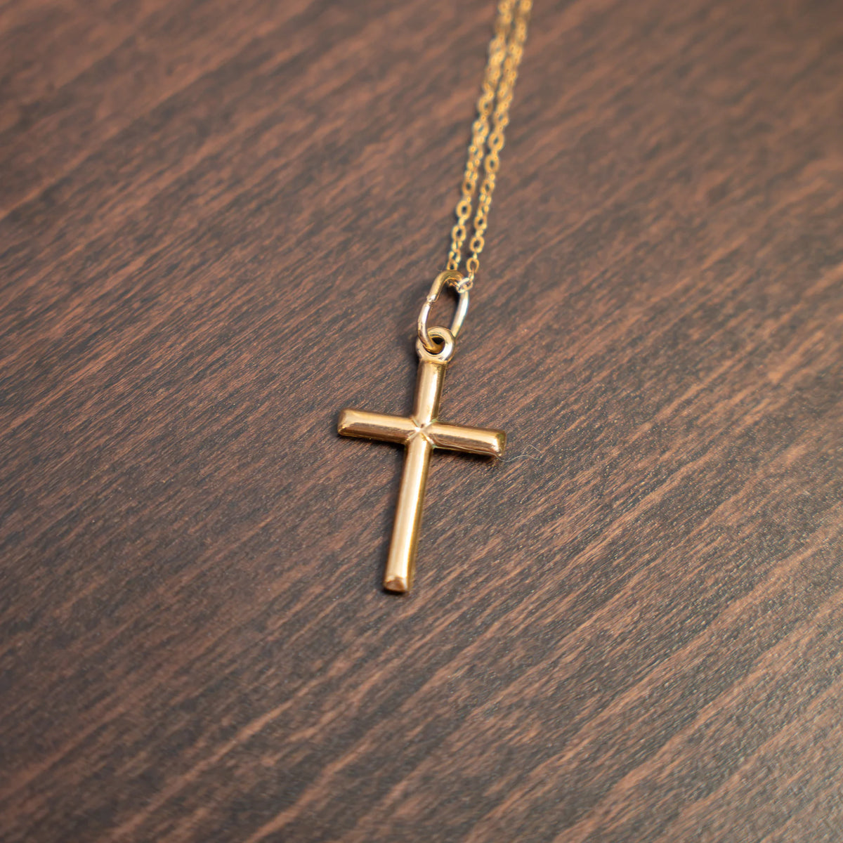 Colgante Cruz Lisa de Plata 925 · 26 × 16 mm en dorado, sobre madera oscura
