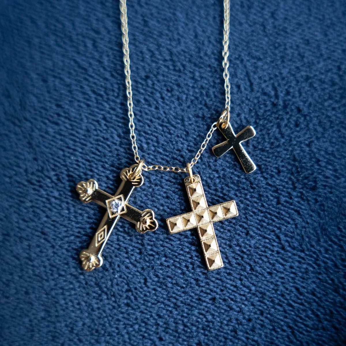 Collar de tres cruces en dorado extendido sobre tela azul, con los tres colgantes a la vista