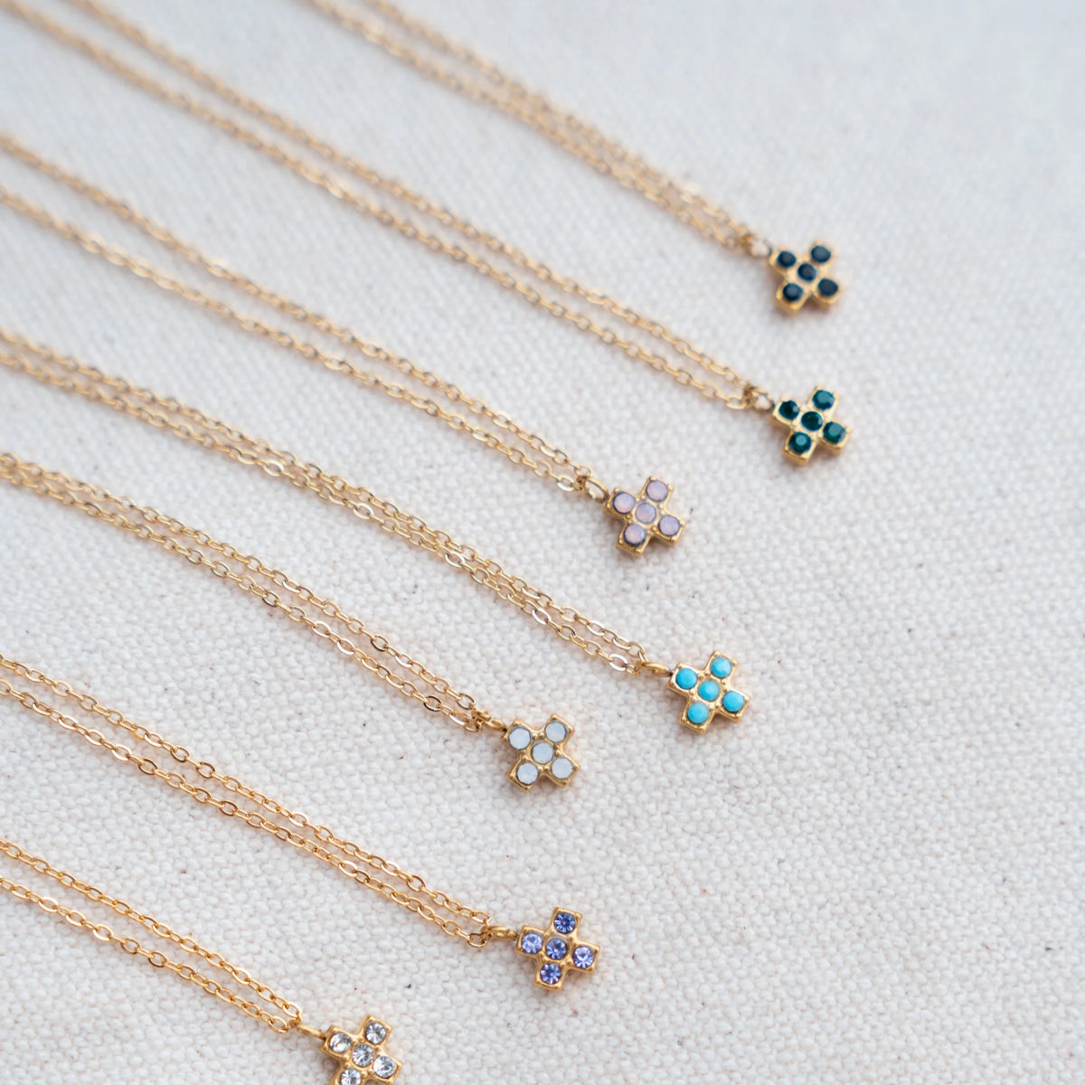 Siete cruces cuadradas de colores con sus cadenas doradas sobre lino