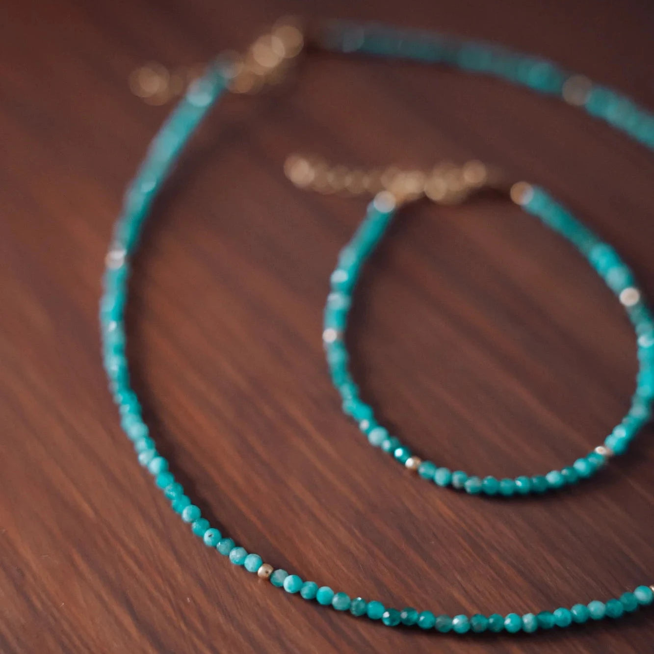 Collar y pulsera de piedras facetadas neo-apatite con efecto bokeh sobre tabla de madera cálida