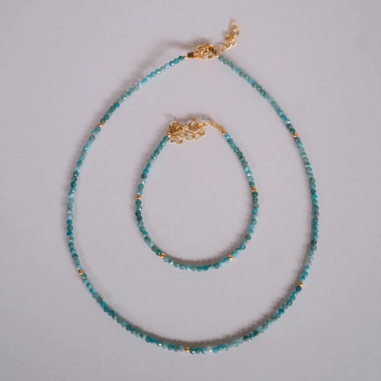 Collar y pulsera de piedras facetadas neo-apatite con separadores dorados sobre fondo gris neutro