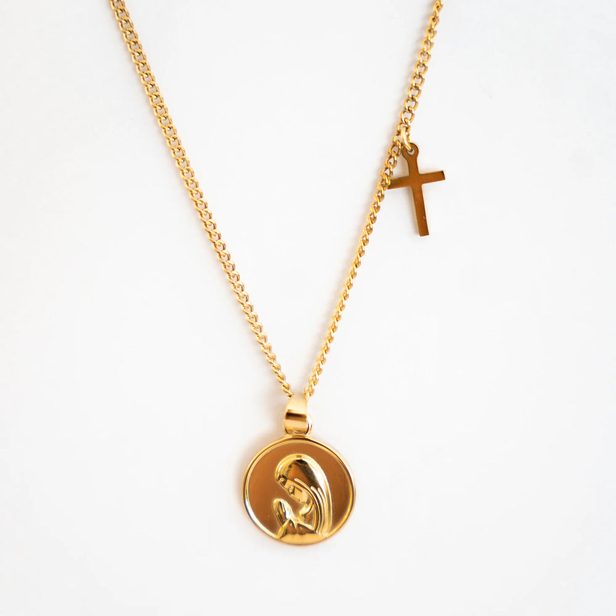 Collar de acero dorado con medalla de la Virgen Niña y pequeña cruz en la cadena, sobre fondo blanco
