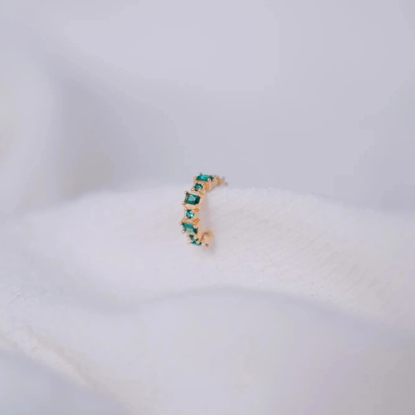 Ear cuff Eclipse esmeralda con circonitas cuadradas alternas en montura dorada sobre superficie esponjosa blanca