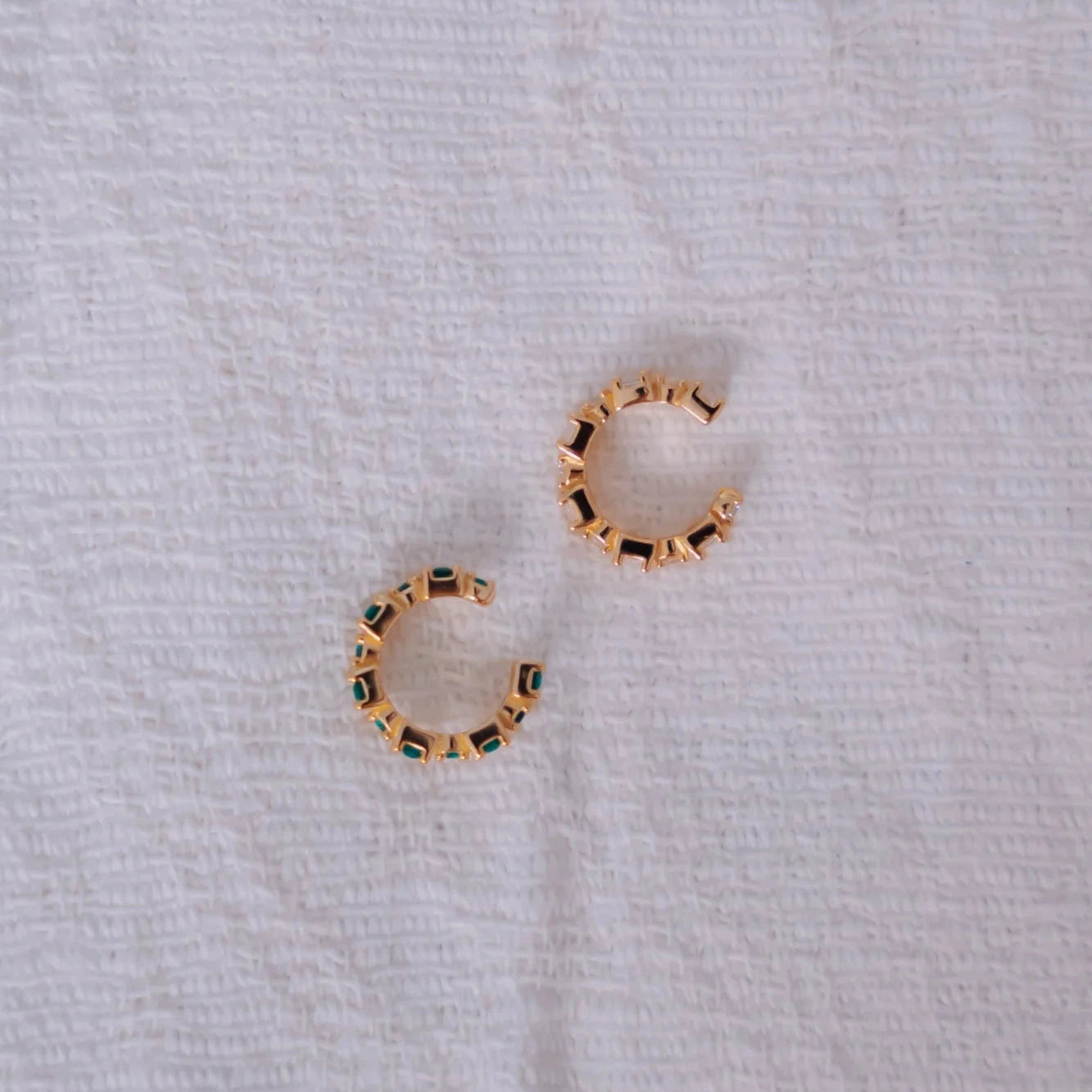 Par de ear cuffs Eclipse esmeralda y blanco vistos desde arriba mostrando su forma en C sobre tela blanca