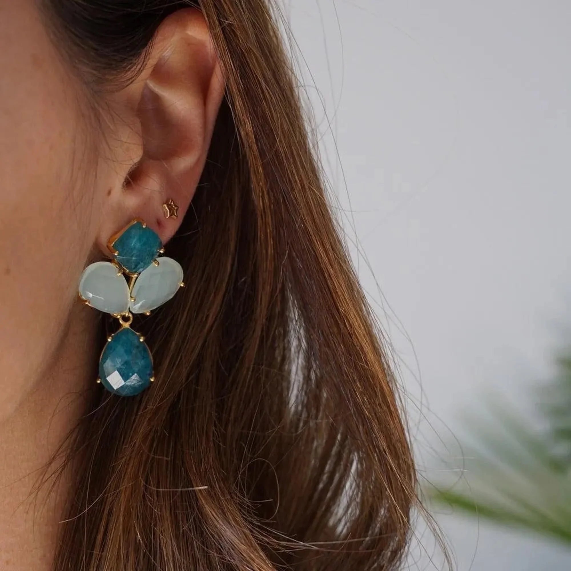Pendiente Estrella Calada dorado junto a un pendiente largo azul en la oreja