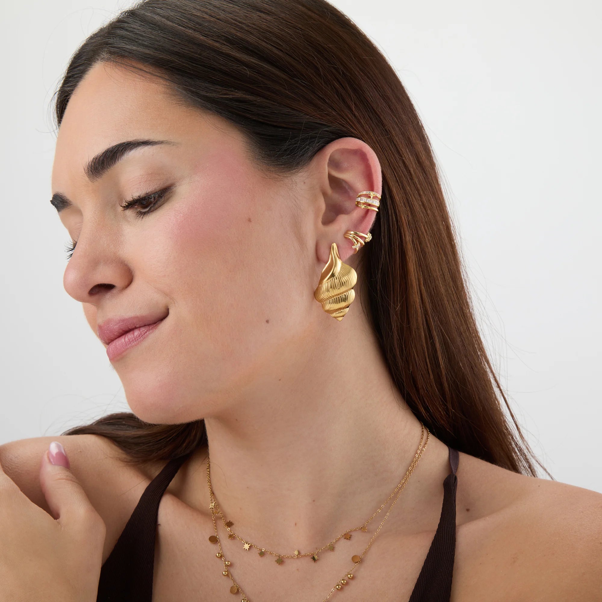 Modelo llevando pendientes caracola dorados junto a un anillo caracola a juego