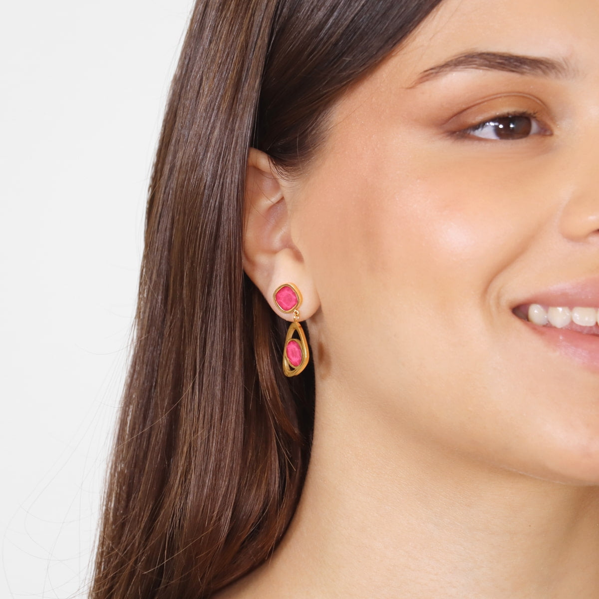 Modelo con pendientes dorados y piedra fucsia de forma calada