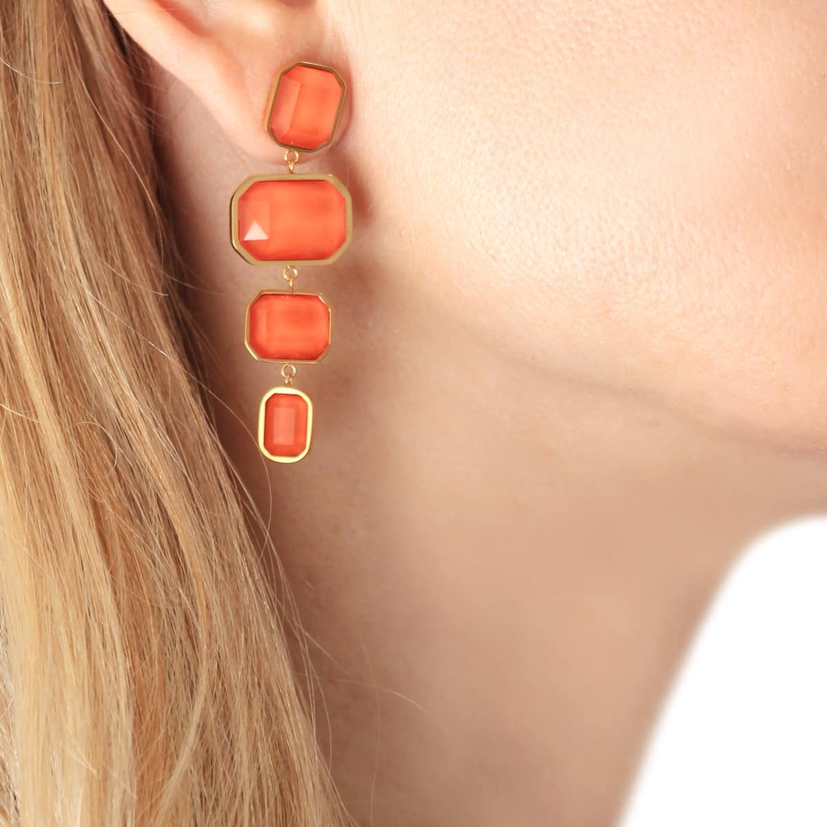 Modelo llevando pendientes largos con cristales en tono naranja, mostrando su caída y brillo en un look elegante