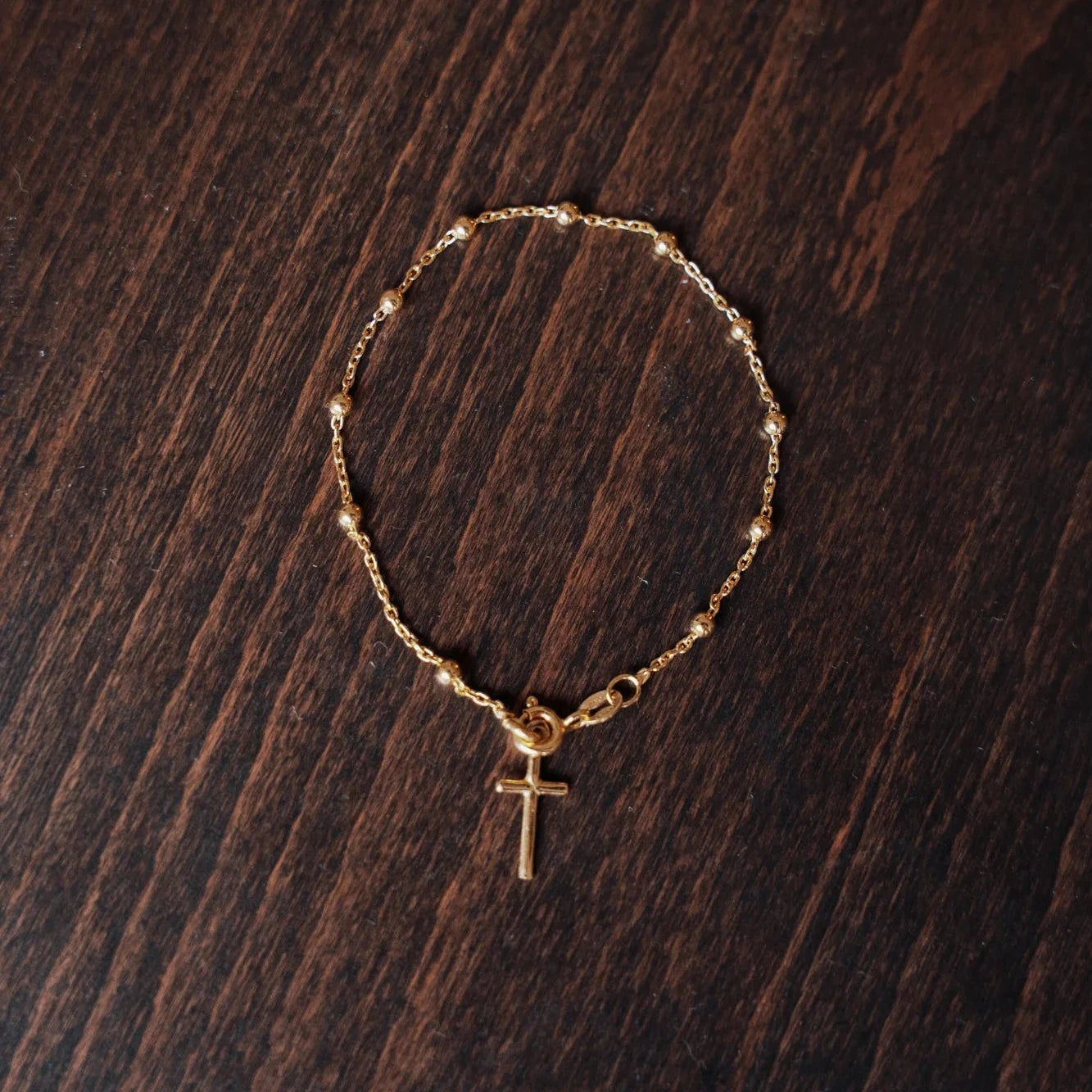 Pulsera decenario de plata de ley chapada en oro 18K con cruz, sobre fondo de madera