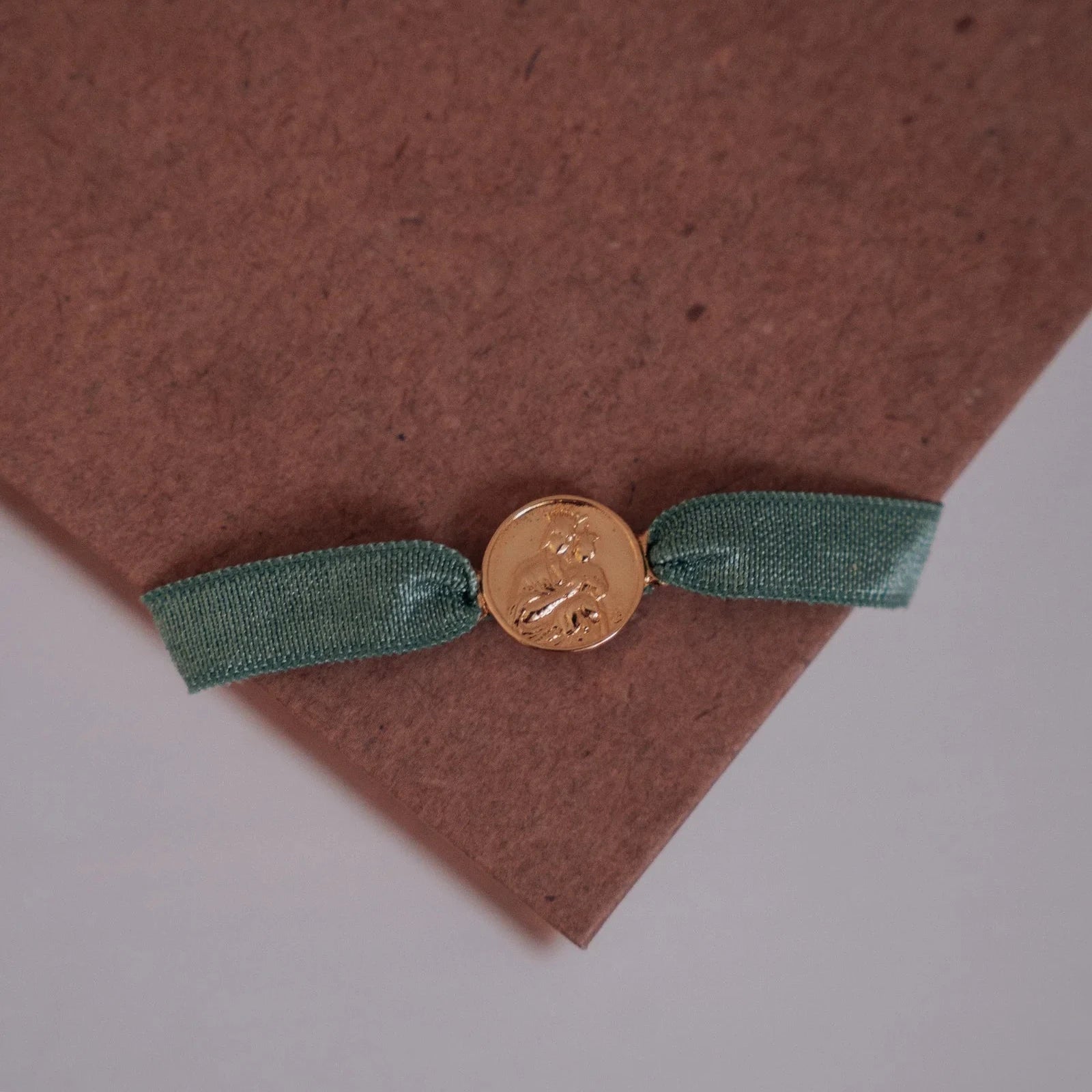Detalle de la medalla dorada de la Virgen del Carmen en la pulsera con cinta verde