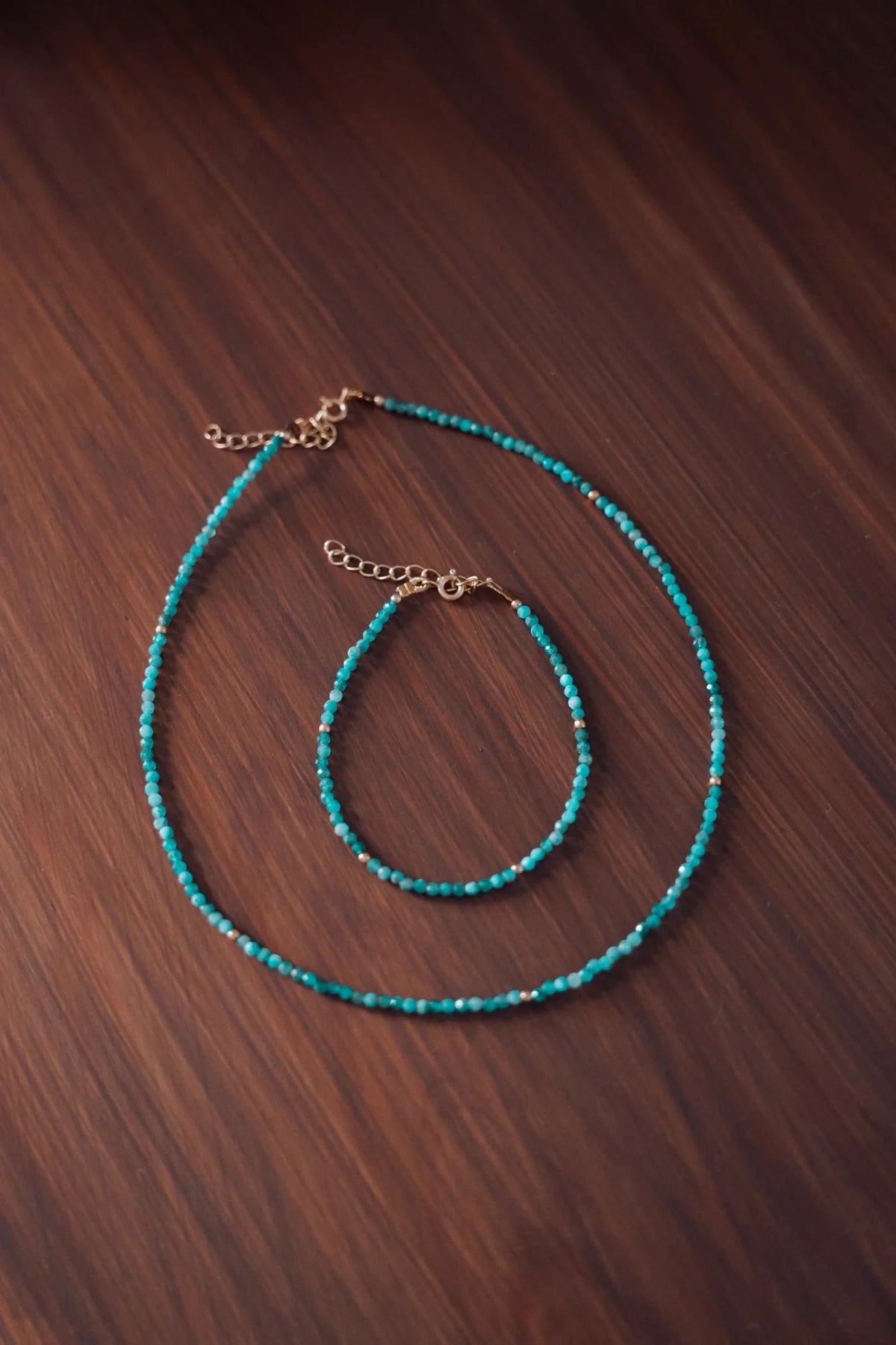 ollar y pulsera de piedras naturales facetadas en turquesa sobre una superficie de madera oscura`