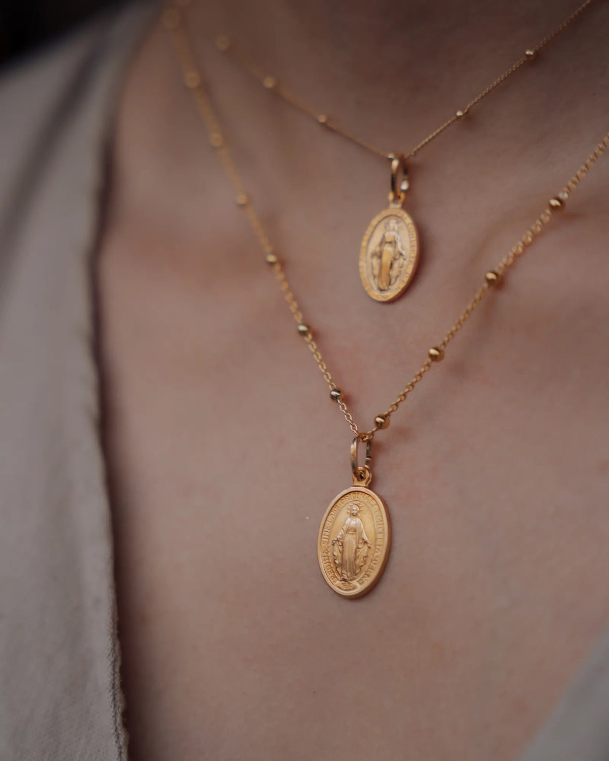 Detalle de dos cadenas de bolas doradas con medallas de la Virgen Milagrosa, puestas a dos alturas