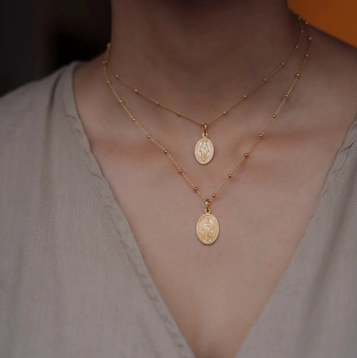 Cadena de bolas dorada puesta junto a otra más larga, cada una con una medalla de la Virgen Milagrosa