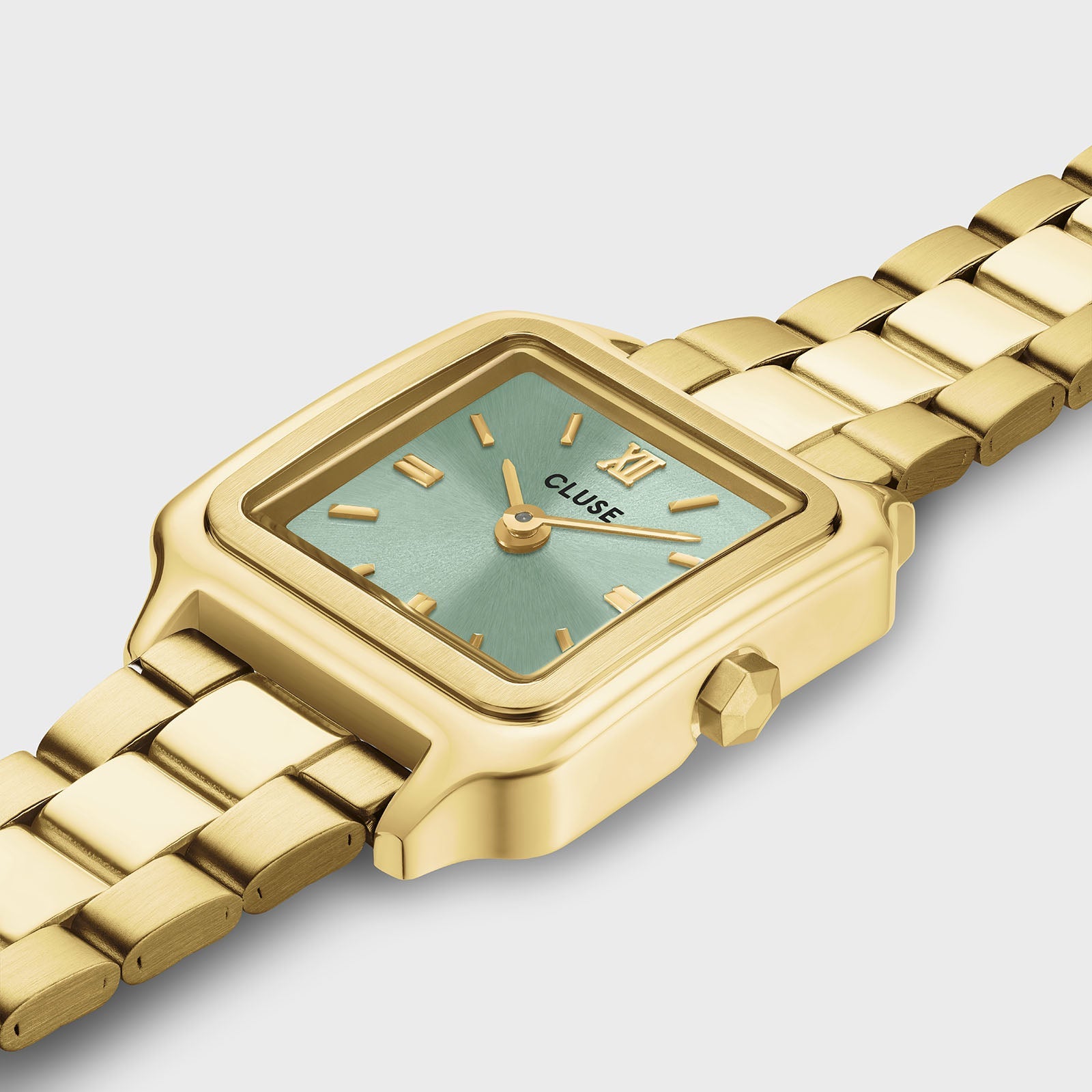 Primer plano del reloj CLUSE Gracieuse Mini: caja de acabado dorado, esfera verde salvia y detalles dorados en un ángulo cercano.
