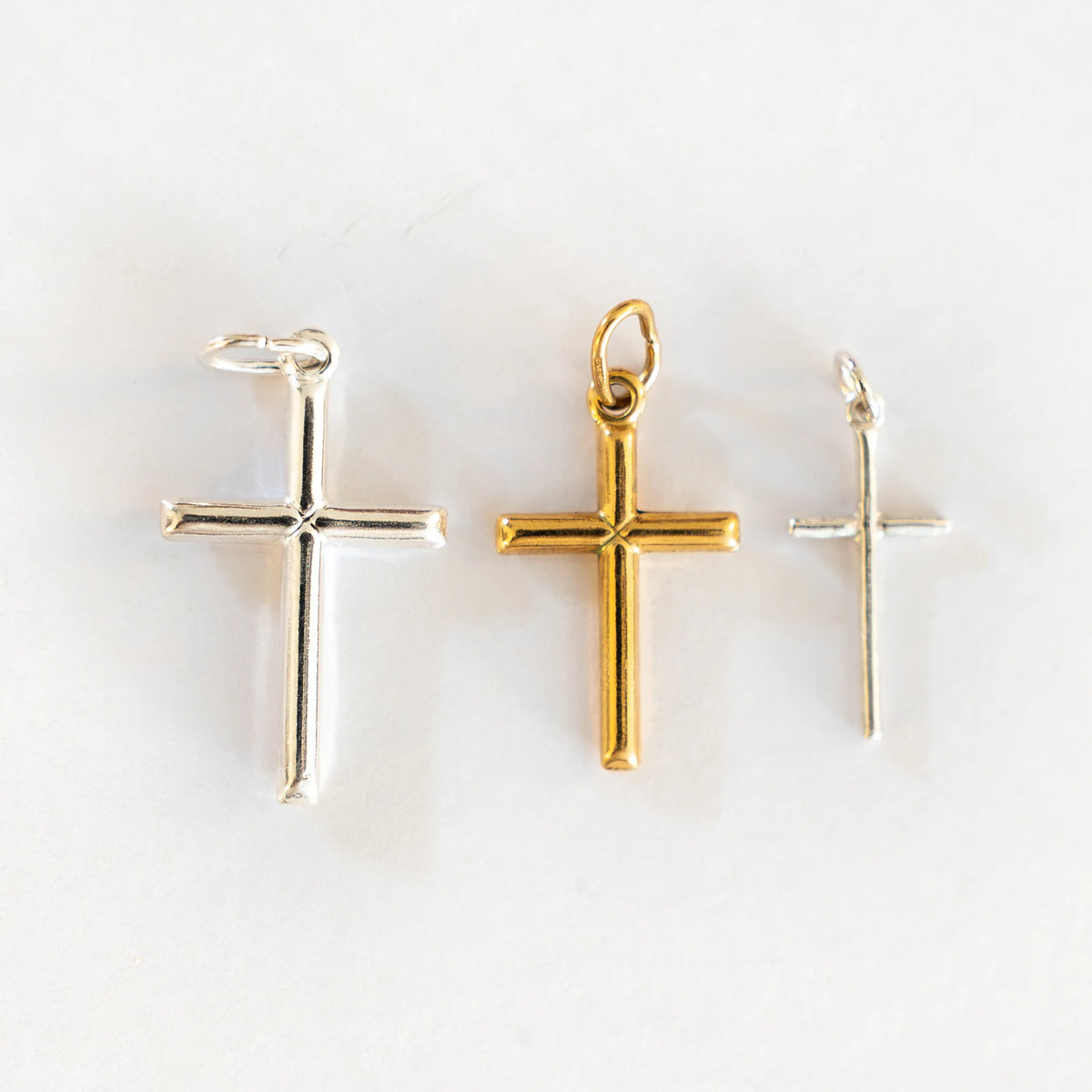 Tres cruces lisas de plata de ley de distintos tamaños, con la de 26 × 16 mm en dorado en el centro