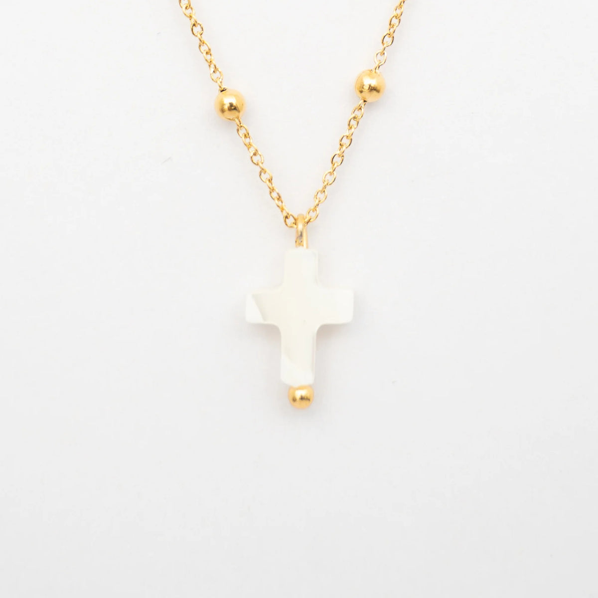 Collar con cruz de nácar blanca y cadena dorada de bolitas sobre fondo claro