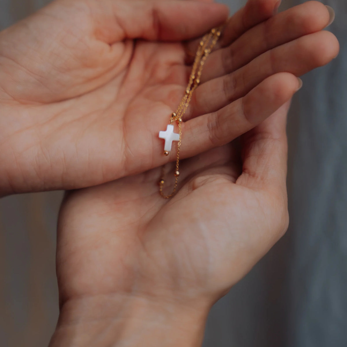 Manos sosteniendo la cruz de nácar con su cadena de bolitas dorada