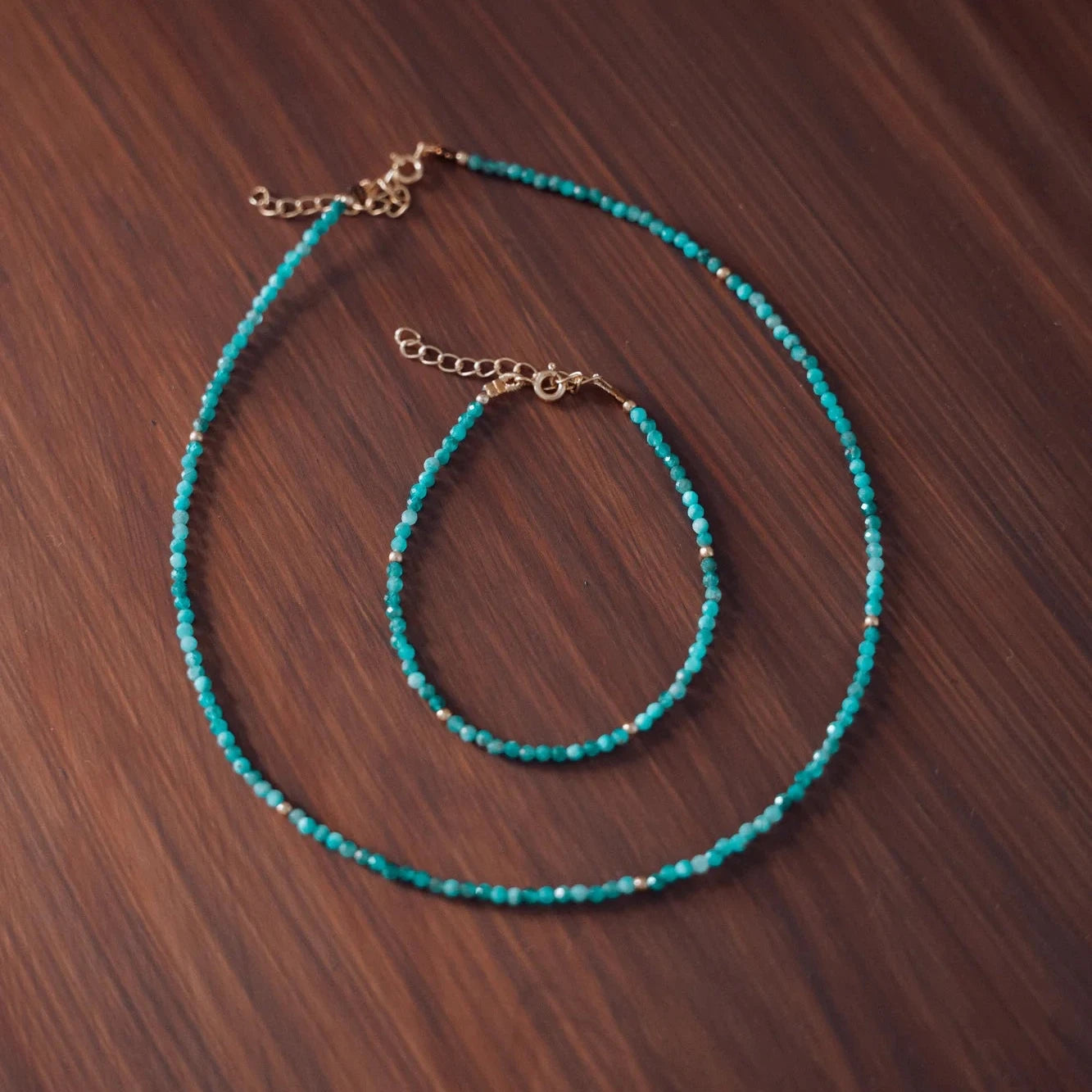 Collar y pulsera de piedras facetadas neo-apatite azul verdoso con separadores dorados sobre madera oscura