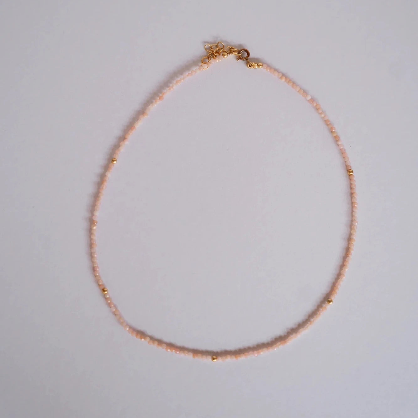 Collar de piedras facetadas ópalo rosa con separadores dorados sobre fondo gris neutro