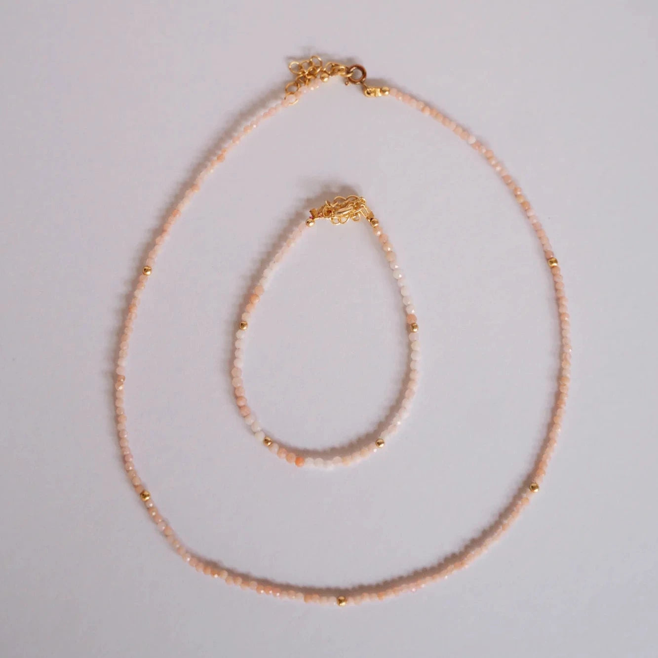 Collar y pulsera de piedras facetadas ópalo rosa con separadores dorados sobre fondo gris