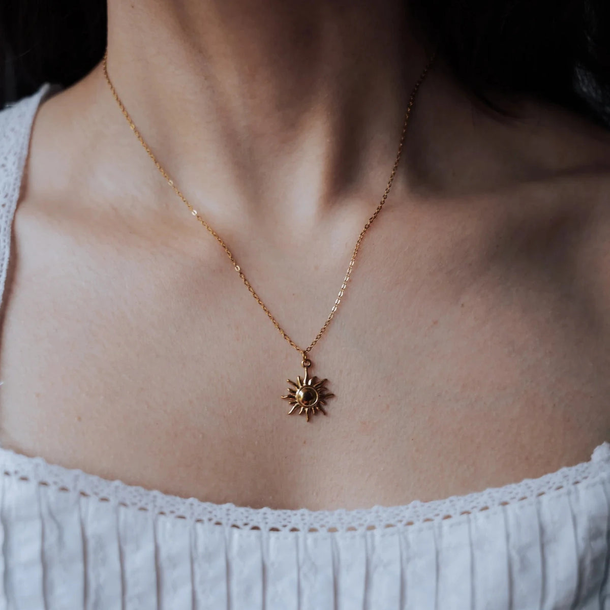 Collar de sol en acero dorado puesto, cayendo sobre blusa blanca de escote cuadrado