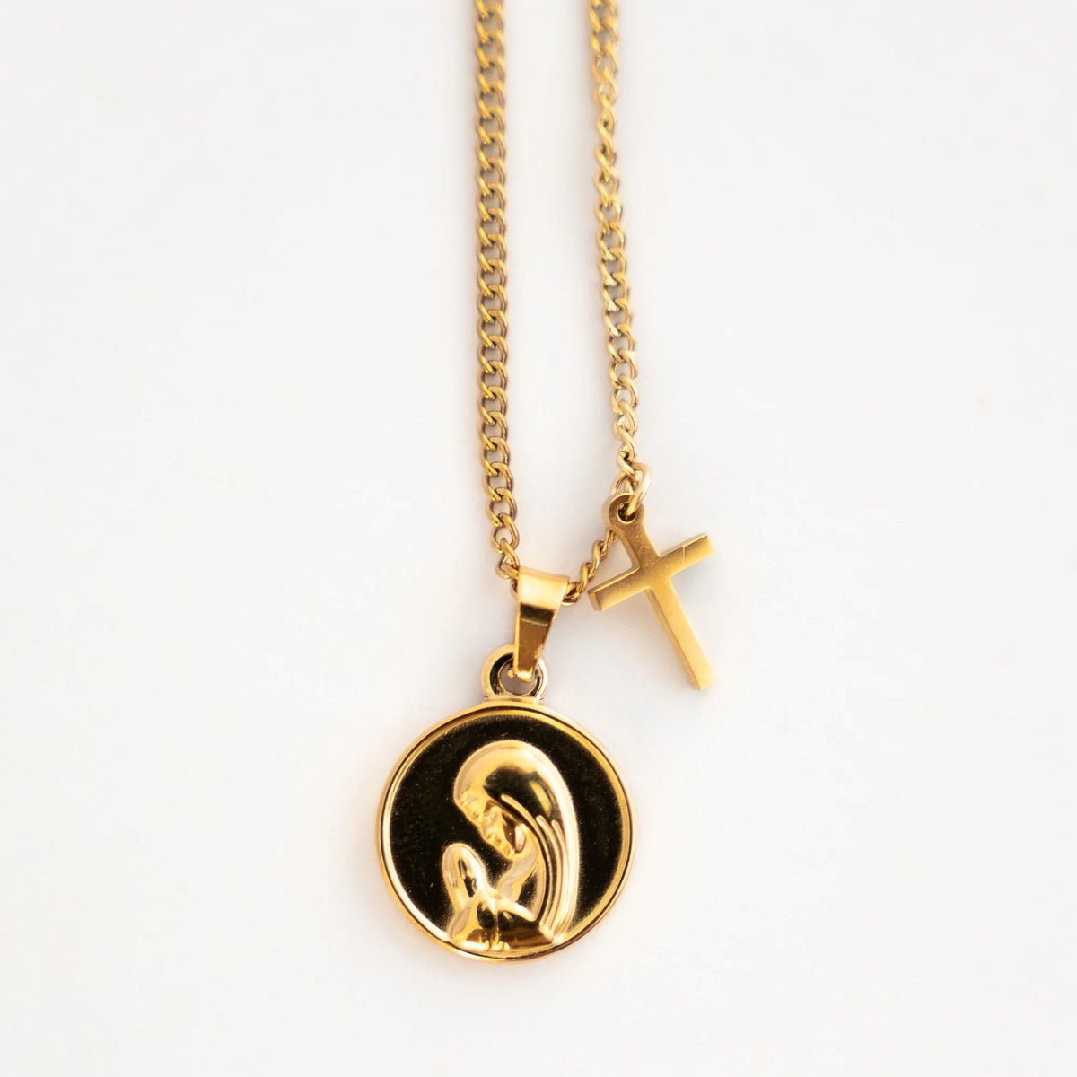 Detalle de la medalla de la Virgen Niña y la cruz del collar de acero dorado