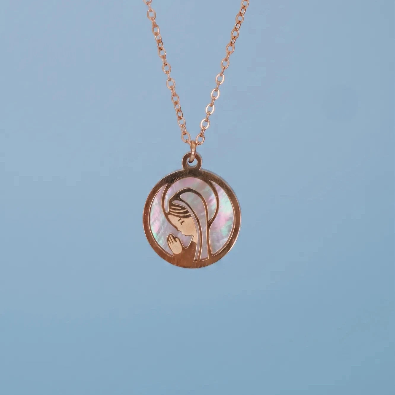 Colgante circular de la Virgen Niña en acero dorado con nácar sobre fondo azul suave