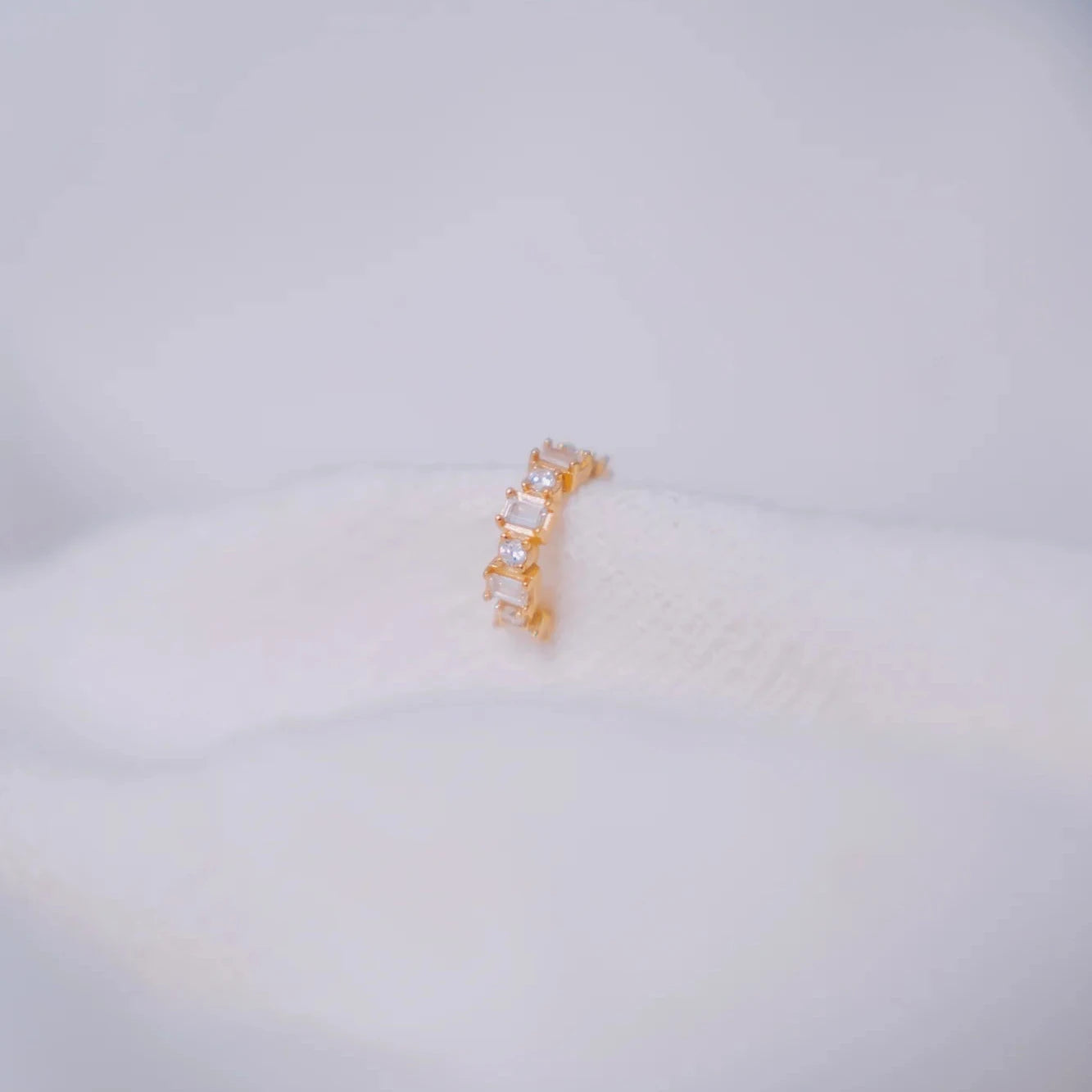 Ear cuff Eclipse blanco con circonitas cuadradas y redondas en montura dorada sobre superficie esponjosa