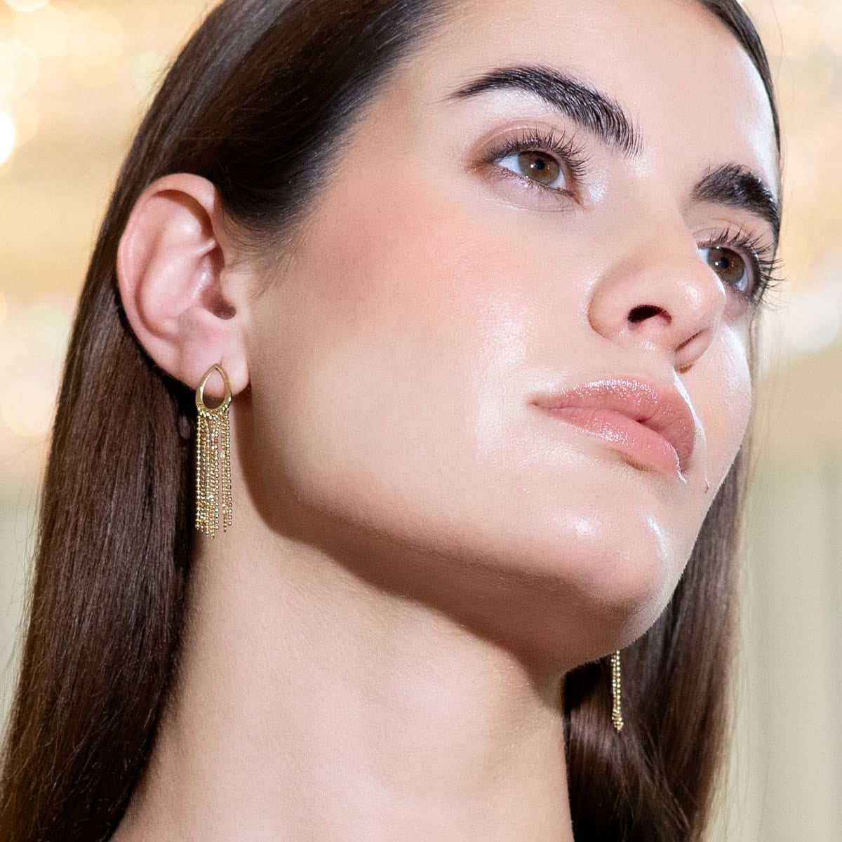Mujer luciendo pendientes largos dorados con cadenas finas, estilo elegante y moderno.