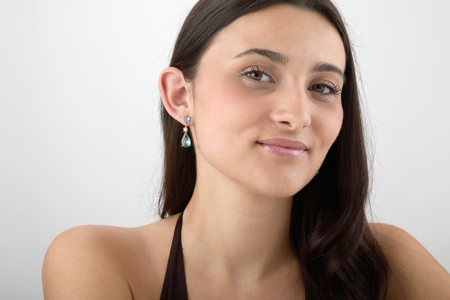 Modelo llevando pendientes Aura Doble Gota con circonitas azules y acabado dorado