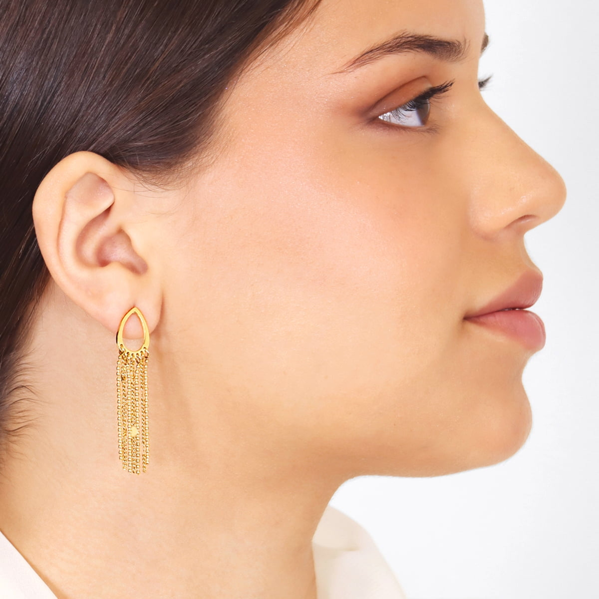 Pendientes dorados con forma de lágrima y cadenas colgantes vistos puestos en la oreja.