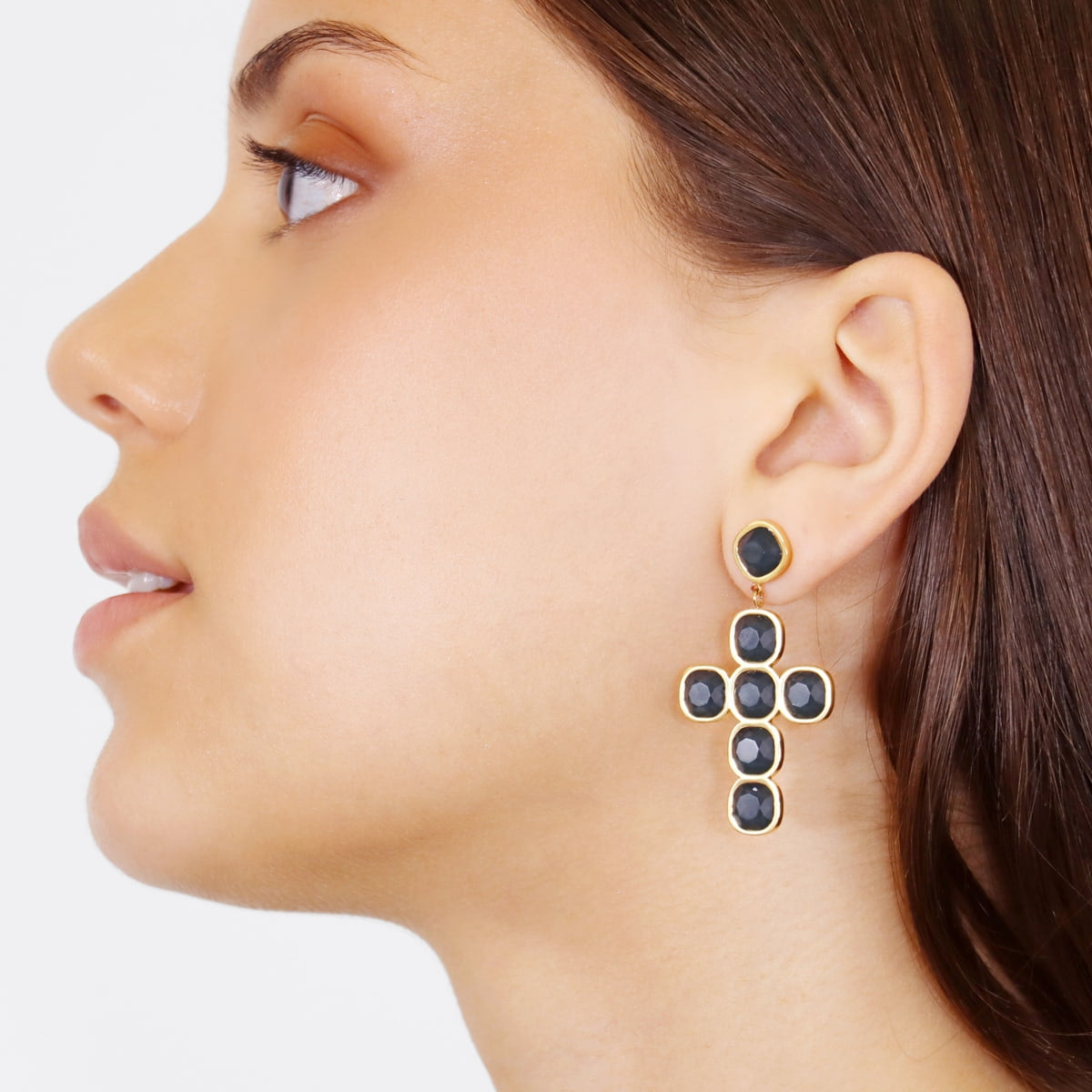 Modelo con pendientes en cruz dorada y piedras negras facetadas

