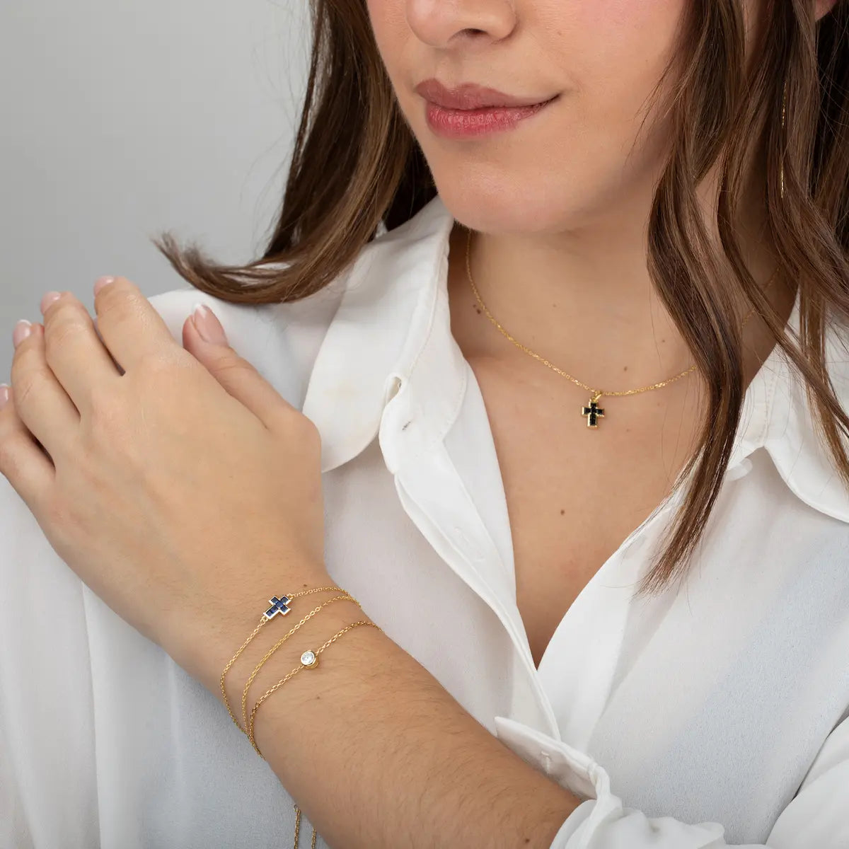 Modelo luciendo a pulsera cruz brillante de plata de ley con baño de oro en tono azul