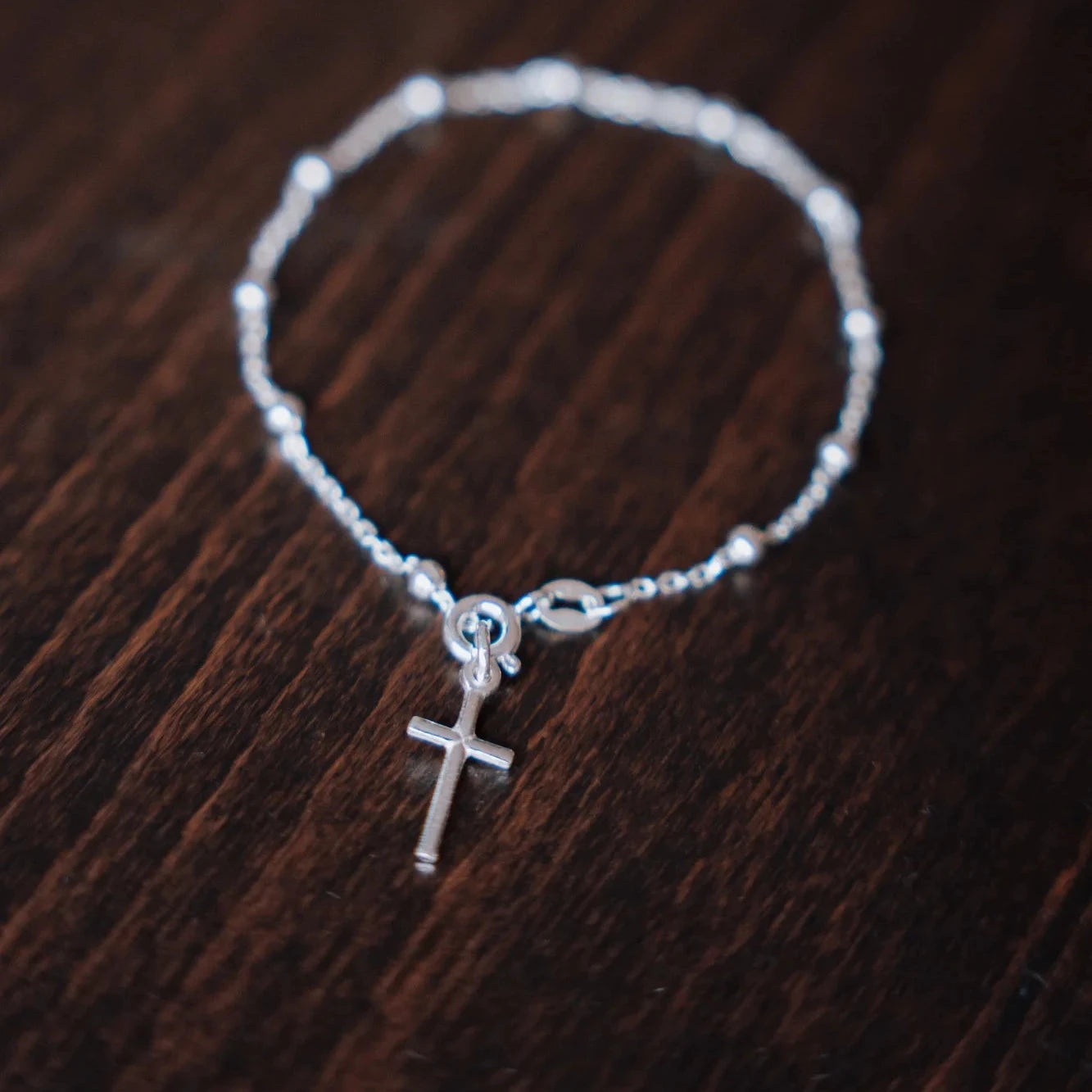 Pulsera decenario de plata de ley con cruz, acabado plateado, sobre fondo de madera
