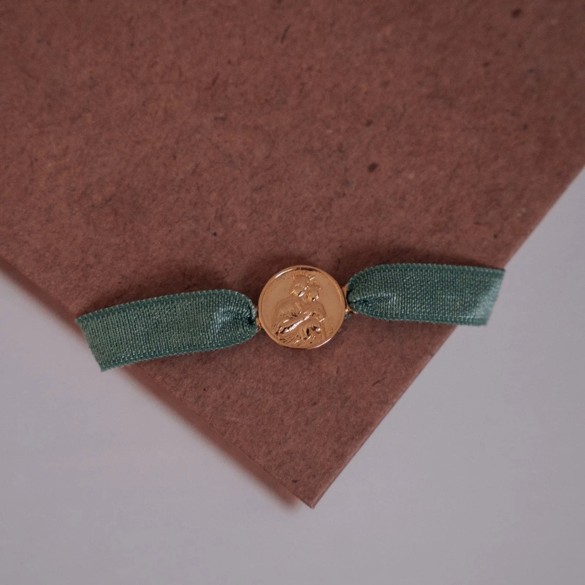 Detalle de la medalla dorada de la Virgen del Carmen en la pulsera con cinta verde