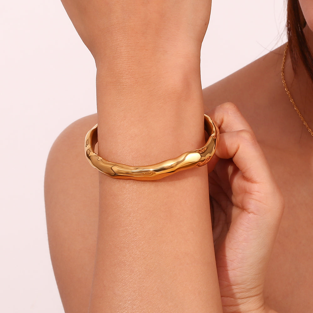 Pulsera esclava dorada martilleada puesta en la muñeca, acabado texturizado