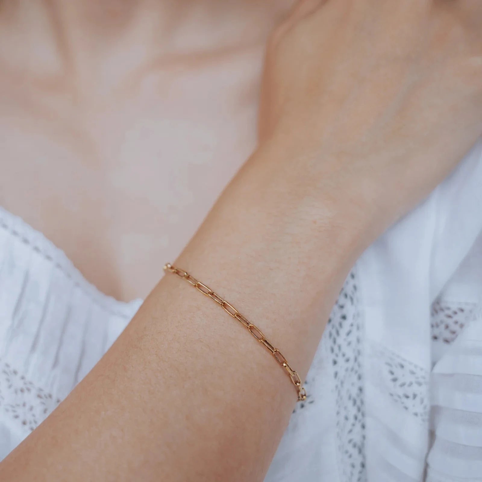 Pulsera de eslabones dorada puesta en la muñeca, sobre blusa blanca