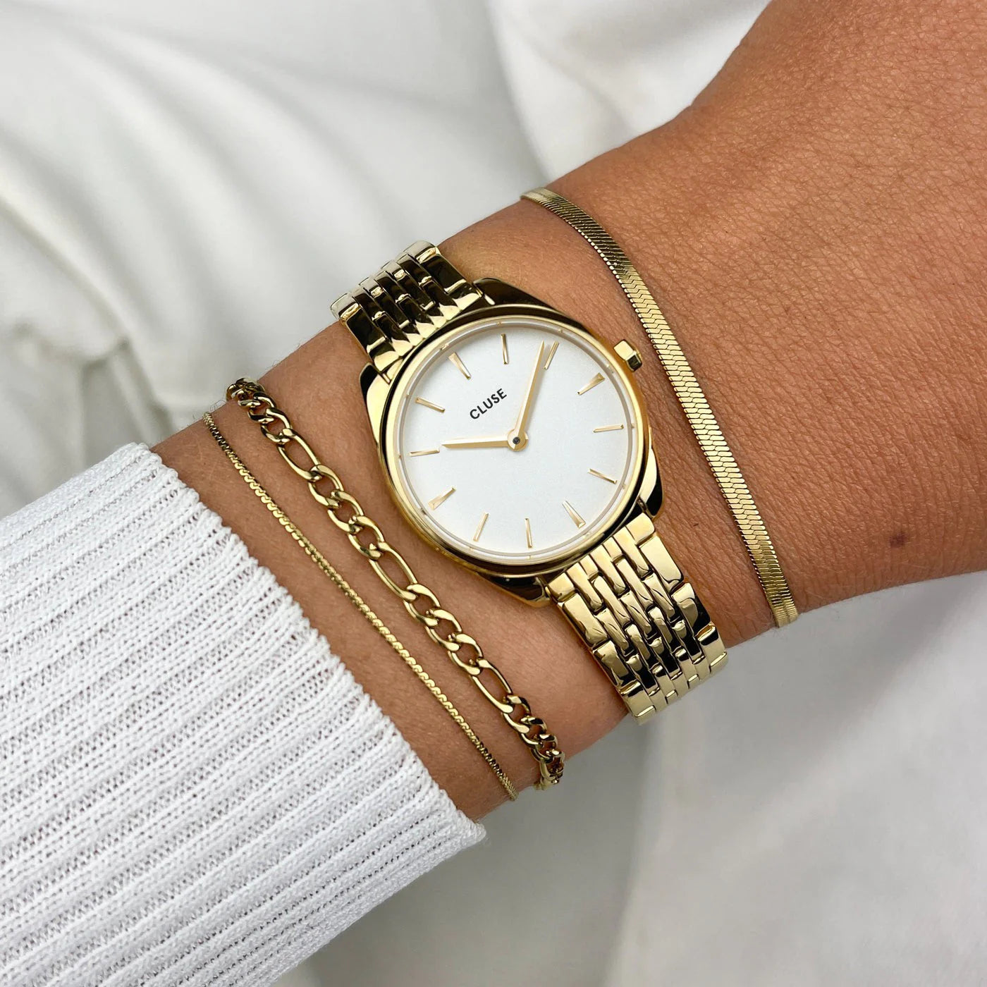Reloj Cluse Féroce Mini White Gold puesto en muñeca, combinado con pulseras doradas